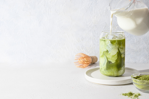 Iced Green matcha tea and pouring milk in glass on white background.Close up. Horizontal orientation.