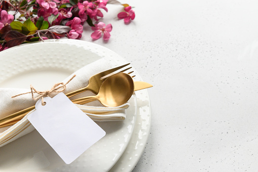 Elegance table setting with apple tree flowers, golden cutlery and tag on white table. Close up. Space for text.