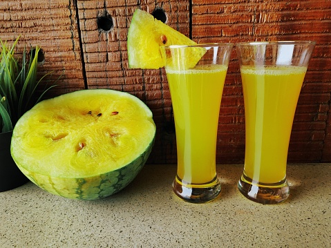 Fresh yellow watermelon juice with sliced watermelon in a wooden background