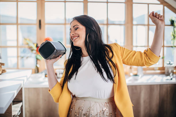 istock Woman singing and dancing at home and holding wireless bluetooth speaker 1227397766