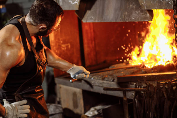 young traditional caucasian blacksmith working with open fire in workshop