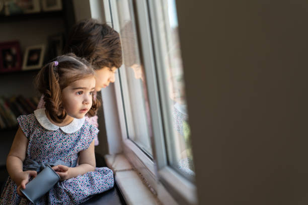 bambino di sette anni che guarda attraverso la finestra insieme alla sorella durante l'eid in turchia - 6 7 years little girls child portrait foto e immagini stock