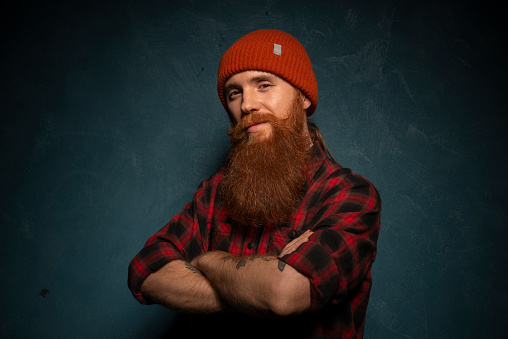 Red bearded man with orange hat and plaid shirt on the dark cyan background