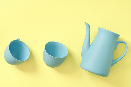 minimalism concept with light pastel colored blue teapot and cups on yellow background.  Flat lay. Tea time concept. Empty space