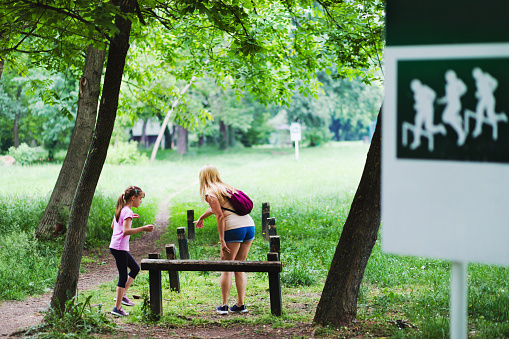 Girl and her mother are walking outdoors in the park, doing workouts.