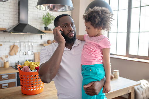 Phone call. Dark-skinned tall father holding his kid and talking on the phone