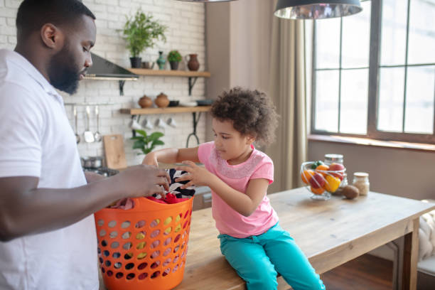 istock Dark-skinned tall father and his cute daughter sorting clothes for washing 1227404387
