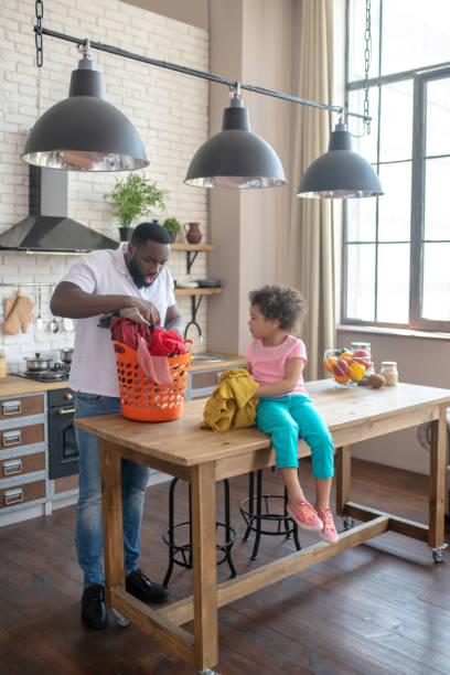 istock Dark-skinned tall father and his cute daughter looking busy with housework 1227404390