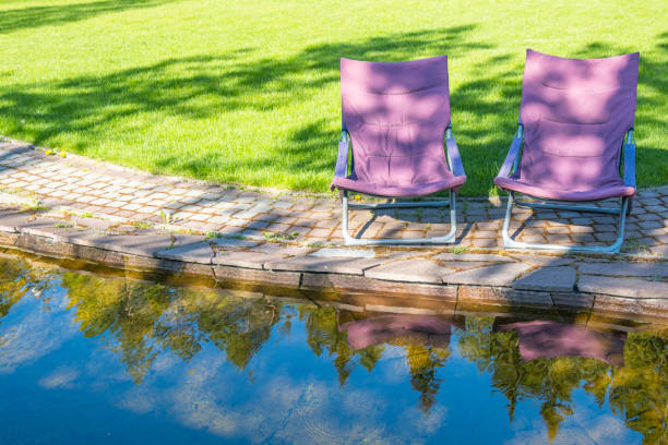 Two deck chairs on fresh green lawn by pond in backyard on summer sunny day