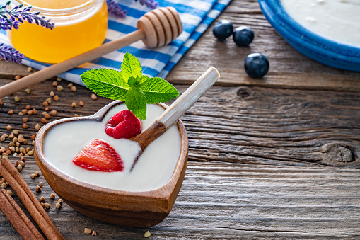 Homemade yogurt heart shape wooden bowl with mint leaves and glass container on rustic wooden board table for healthy breakfast