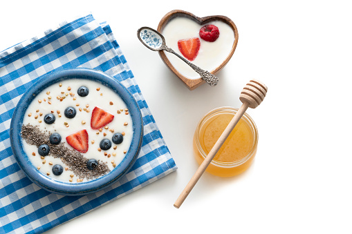 Homemade yogurt blue bowl healthy breakfast with chia strawberries blackberries heart shape and honey isolated on white background