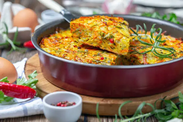 Vegetable Kugel of zucchini, carrots, potatoes, garlic and turmeric in a round baking dish, selective focus. Dish of traditional Jewish cuisine.