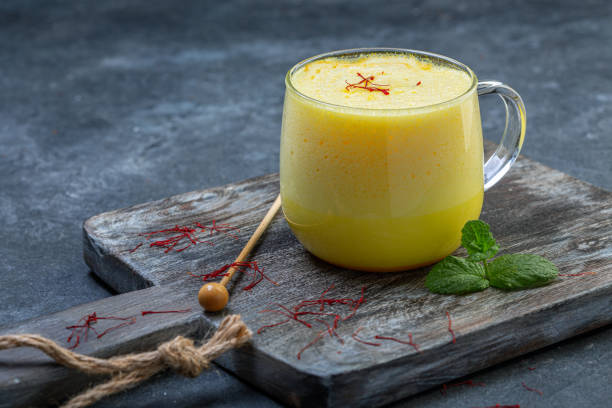 Saffron latte with almond milk. Trendy healthy food drink latte with saffron and almond milk in a glass cup served on a wooden serving board, selective focus. saffron stock pictures, royalty-free photos & images