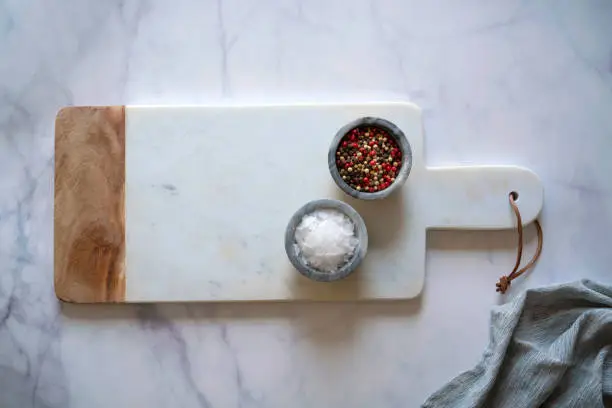 White Marble cutting board on white marble counter with salt and pepper spices monochromatic kitchen food background with copy space