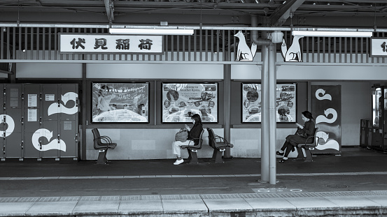 Two women are sitting at a train station, looking at their phones while waiting to the train, Kyoto, Japan.