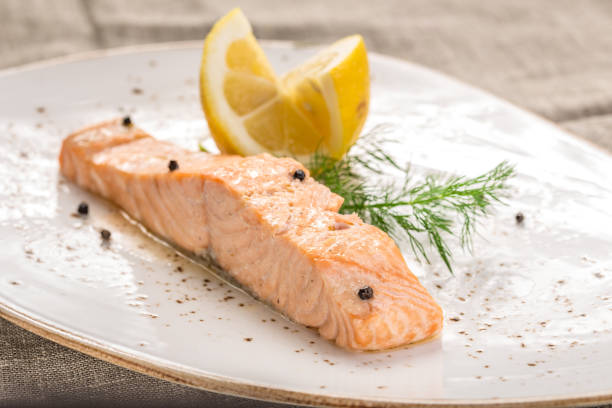 Steamed salmon with lemon on white plate on grey tablecloth stock photo