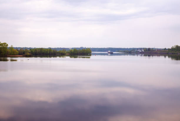 Russian landscape, Volga river in morning at dawn in light haze. Pink-purple clouds are reflected in calm water. Cargo barge goes upstream of the Volga River, Uglich