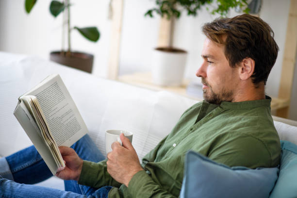 istock Man sitting on sofa and reading book at home, lockdown concept. 1227415629