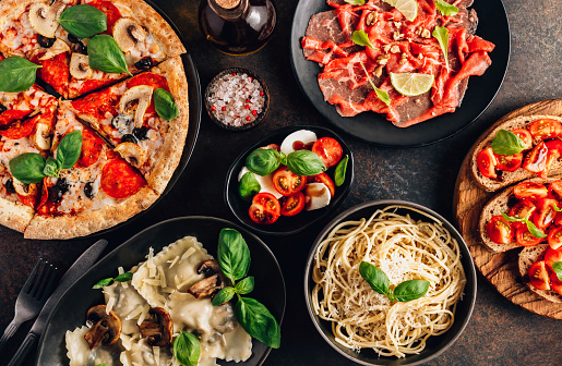 Mesa completa de comidas italianas en platos Pizza, pasta, ravioles, carpaccio. Ensalada caprese y bruschetta de tomate sobre fondo negro. photo