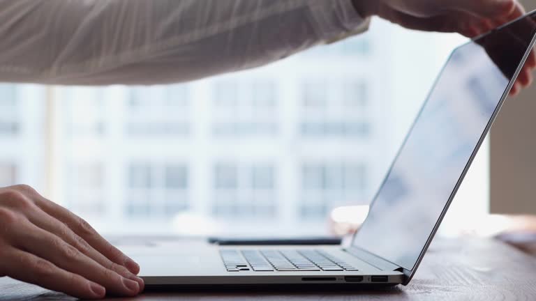 Close-up of hands of unrecognizable man turning off laptop and closing lid.