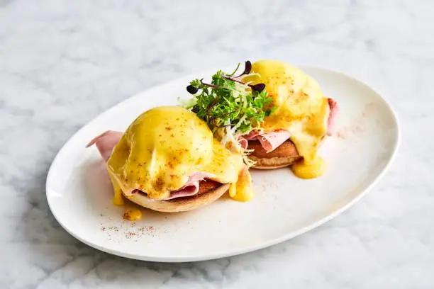 Photo of eggs Benedict with arugula, bacon and hollandaise sauce on gray wooden background.