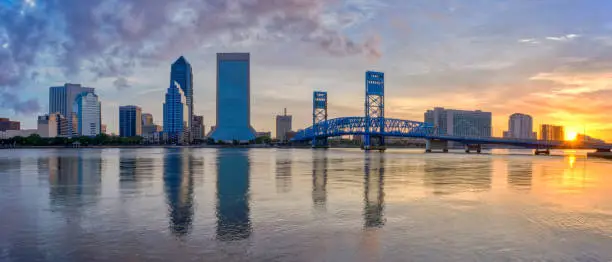The downtown skyline of Jacksonville, Florida during sunrise.  The view is from the Southbank Riverwalk area and features the St. Johns River and the John T. Alsop Jr. Bridge.