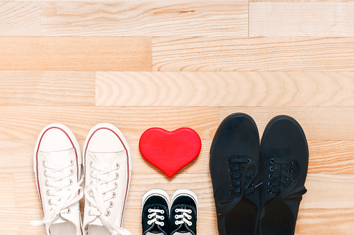 Happy family concept. Father, mother and little kid shoes on wooden floor with red heart. Symbol of family growth, fun, love, togetherness, warmth and care. Top view. Space for text