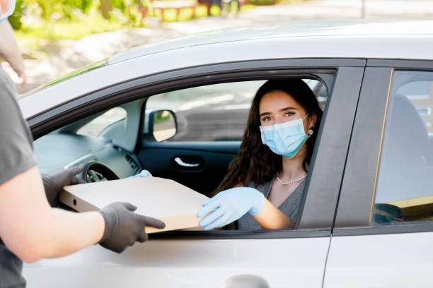 mensajero de entrega de alimentos da pizza a la mujer en coche ecológico. alimentos de seguridad entregados según la distancia social. pizza sabrosa con salami, queso, tomates en caja de cardoard. dar comida por la ventana del auto. - cardoard fotografías e imágenes de stock