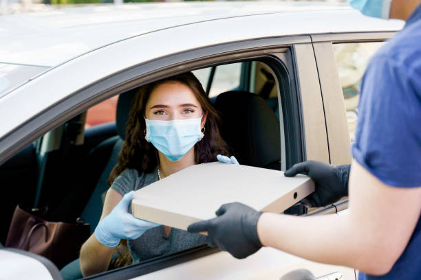 mensajero de entrega de alimentos da pizza a la mujer en coche ecológico. alimentos de seguridad entregados según la distancia social. pizza sabrosa con salami, queso, tomates en caja de cardoard. dar comida por la ventana del auto. - cardoard fotografías e imágenes de stock