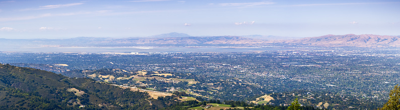 Panoramic view of Silicon Valley, with office buildings close to the bay, surrounded by residential areas; Hills and valleys in Santa Cruz mountains in the foreground; California