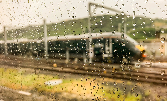 Swansea, Wales - July 2018: Close up of raindrops on the window of a railway carriage, with an high speed express train blurred in the background