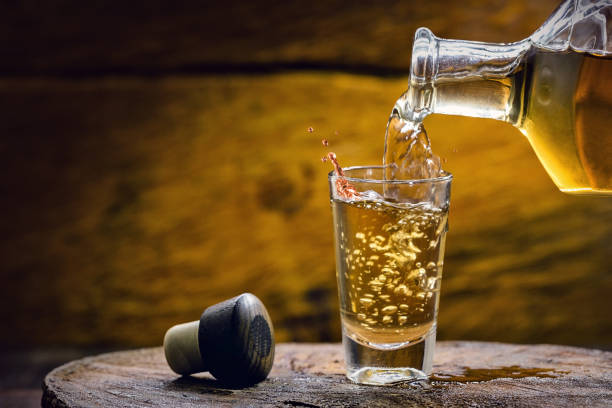 Glass of golden rum, with bottle. Bottle pouring alcohol into a small glass. Brazilian export type drink Glass of golden rum, with bottle. Bottle pouring alcohol into a small glass. Brazilian export type drink distillation photos stock pictures, royalty-free photos & images