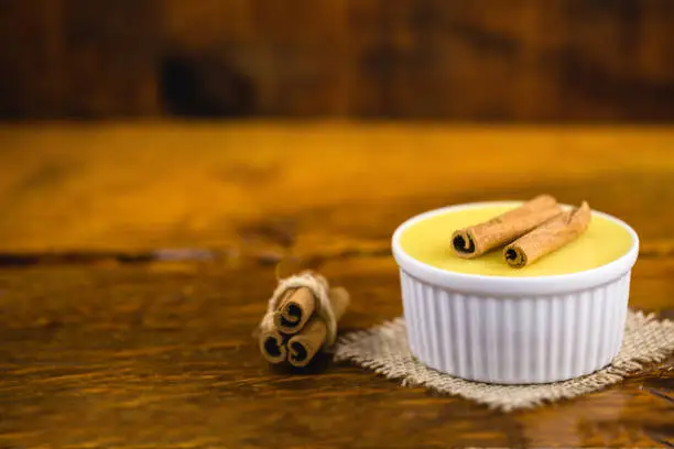 Photo of Brazilian sweet cream-like dessert cured corn mousse with cinnamon on a rustic wooden background. Typical Brazilian cuisine sweet in traditional parties, on a wooden background with copy space.