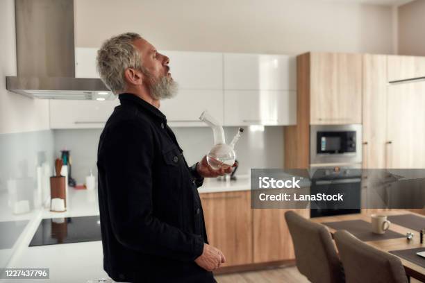 Feel Everything Bearded Midleaged Man Holding A Bong Or Glass Water Pipe While Smoking Marijuana Standing In The Kitchen Cannabis And Weed Legalization Concept Stock Photo - Download Image Now