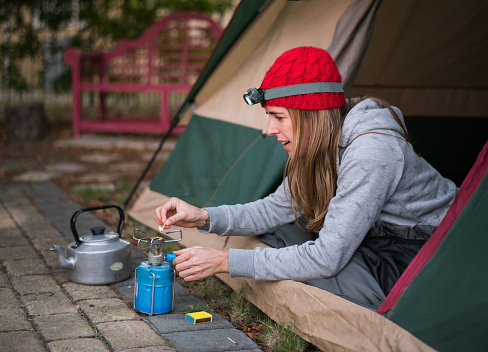 Shot of a woman camping in backyard and igniting the camp stove