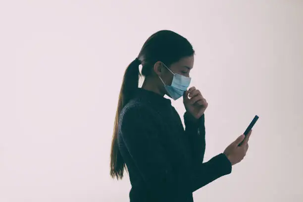 Photo of COVID-19 mask wearing woman touching her face while walking and texting mobile phone, Coronavirus prevention not properly using the protection