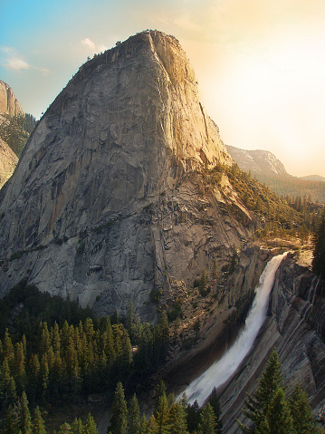 Dramatic Landscape of Half Dome in Yosemite National Park with the setting sun breaking through and illuminated the scene of the rapidly falling Nevada Falls