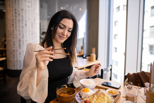 Caucasian woman eating Japanese food 'hamburg steak' for lunch, using chopsticks