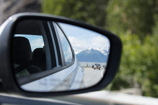 Looking at side mirror on car of road and snow capped Alaska mountain range in background