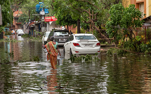 Kolkata, West Bengal, India, May 20, 2020: Woman carrying essential drinking water through water logged city street after massive cyclonic storm Amphan strike at Kolkata, India