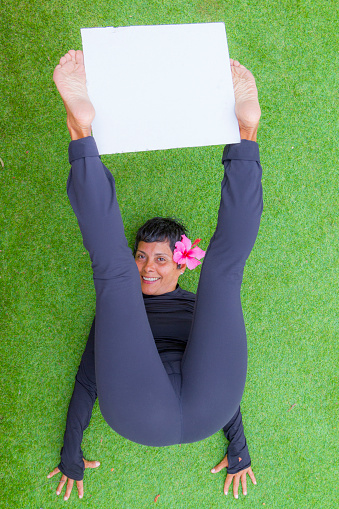 Mature Woman doing pilates exercises at home in Corona Virus Covid-19 quarantine holding a white board.