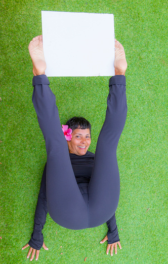 Mature Woman doing pilates exercises at home in Corona Virus Covid-19 quarantine holding a white board.