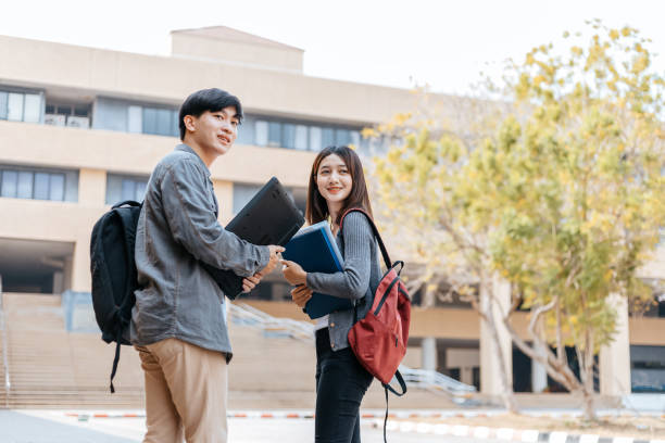 istock high school students hold book and laptop talking and laughing in a hallway between classes 1227465330