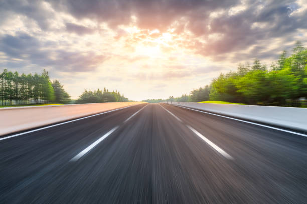 istock Fast moving asphalt highway and green forest at sunset. 1227471348