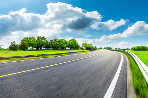 Fast moving asphalt road and green forest with grass landscape.