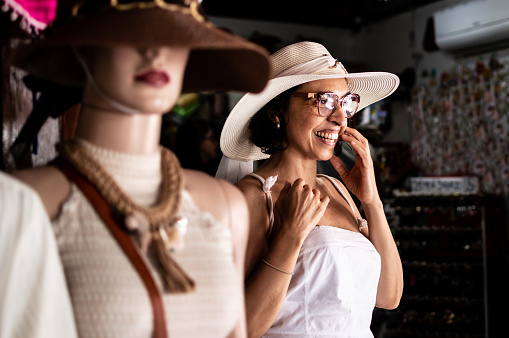 A woman with white dress wearing glasses and hat, next to a mannequin in a shop