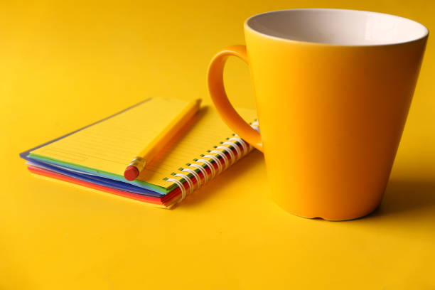 yellow color notepad with pencil and coffee mug on yellow background .
