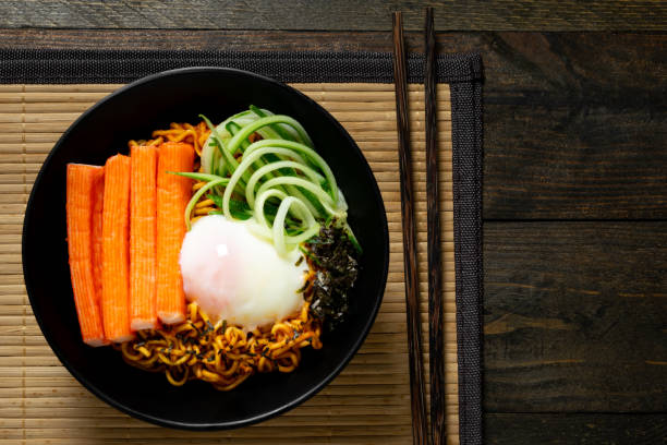 Spicy instant noodle with crab stick and onsen egg and cucumber in black bowl on wooden table. Spicy instant noodle with crab stick and onsen egg and cucumber in black bowl on wooden table. 3686 stock pictures, royalty-free photos & images