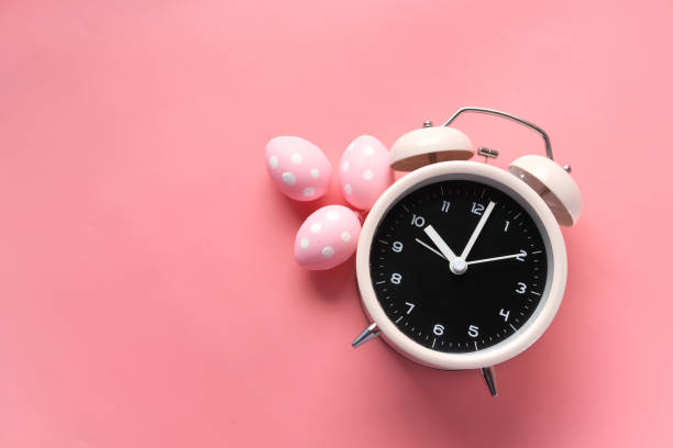 easter concept with alarm clock and eggs on pink background