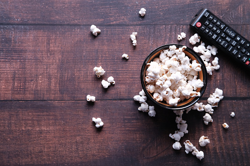 Top view of bowl of popcorn and Tv remote on table .